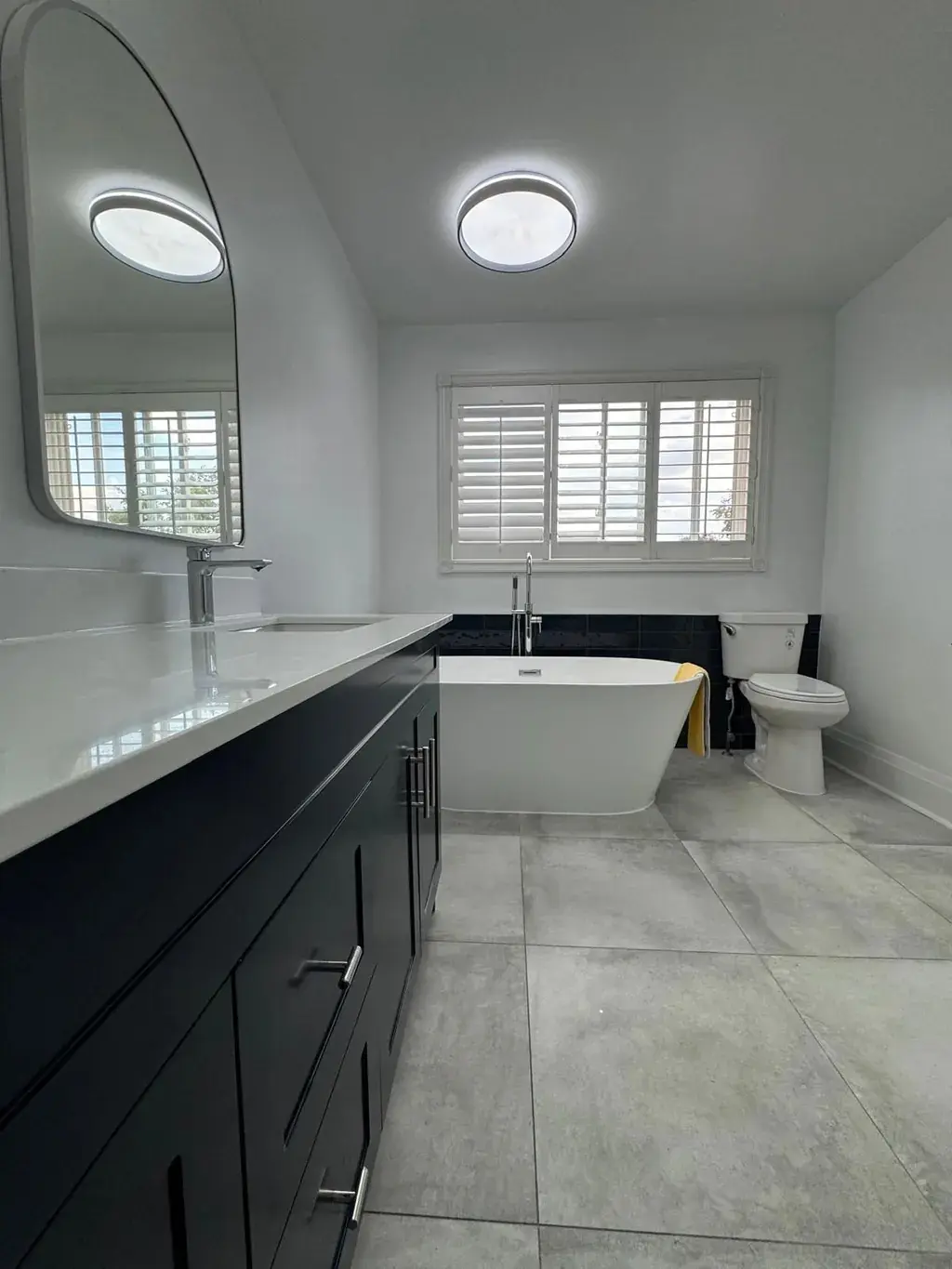 Full bathroom renovation with a black double vanity, freestanding tub and large-format floor tile