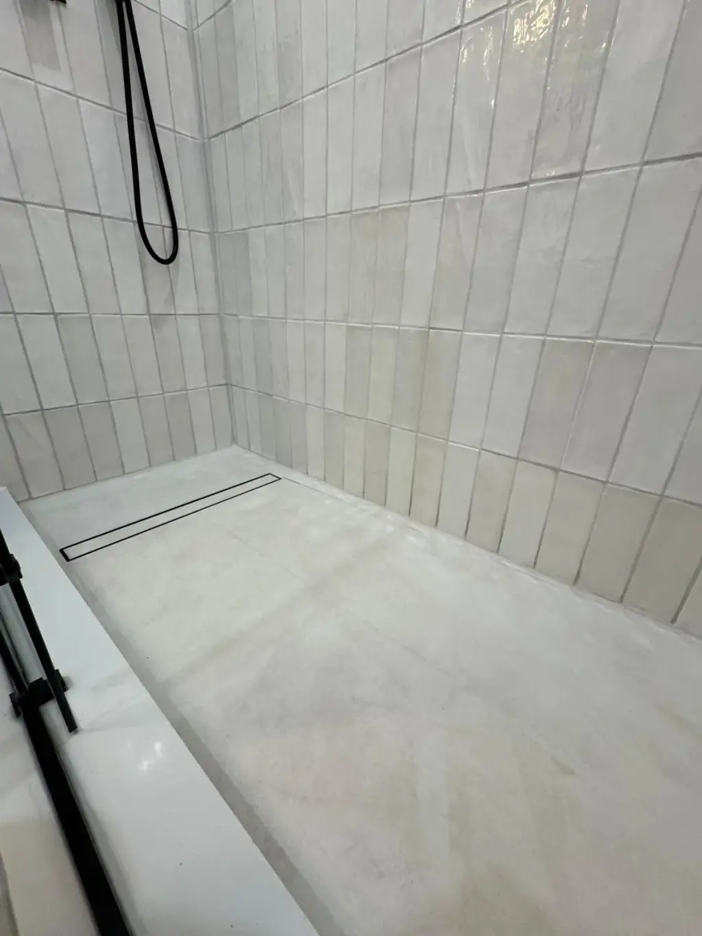 Shower with a Canzeno linear drain base along the back wall, in white tile
