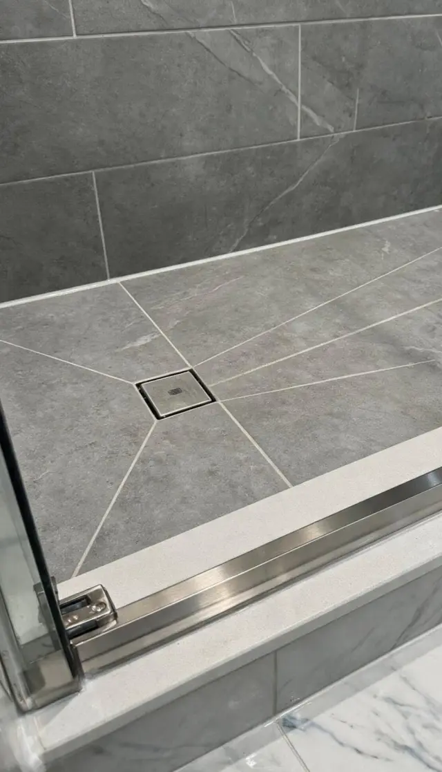 Square drain tiled shower base in grey stone-look tile, with the tile cut to the four-way slope