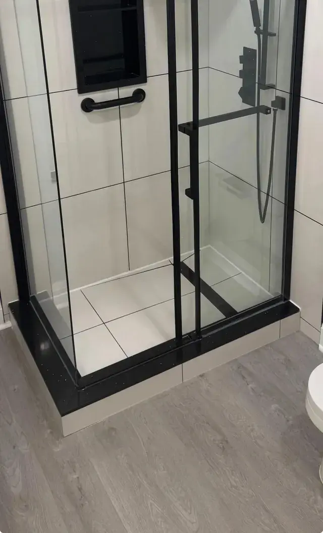 Black-framed glass shower with a tiled base and wall niche