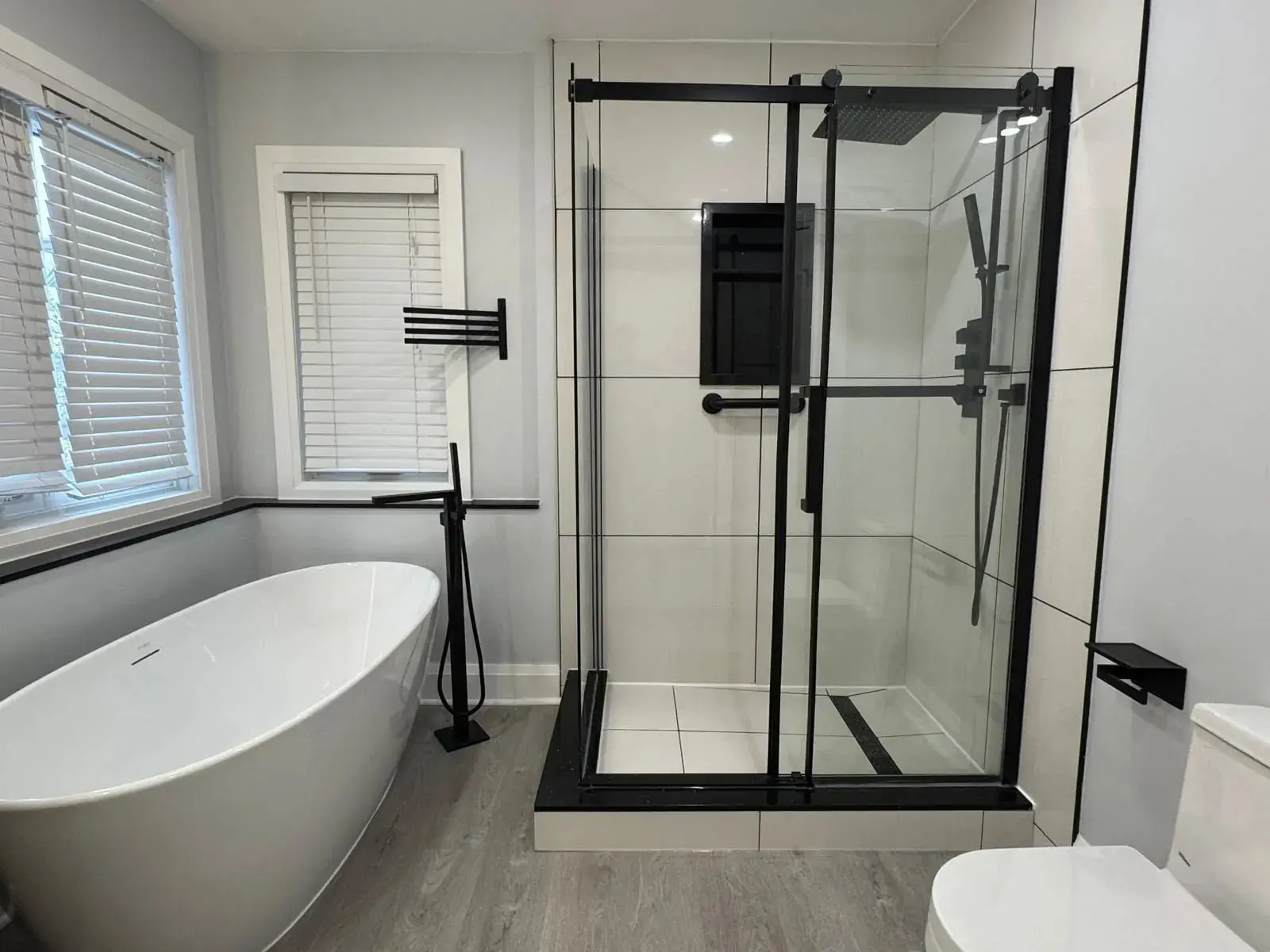 Renovated bathroom in Richmond Hill with a black-framed glass shower on a Canzeno tiled base and a freestanding tub