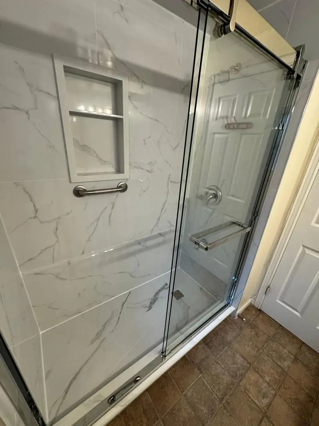 Walk-in shower with a recessed niche, marble-look tile and a sliding glass door