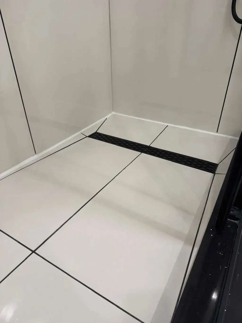 Linear drain along the back wall of a white tiled Canzeno shower base