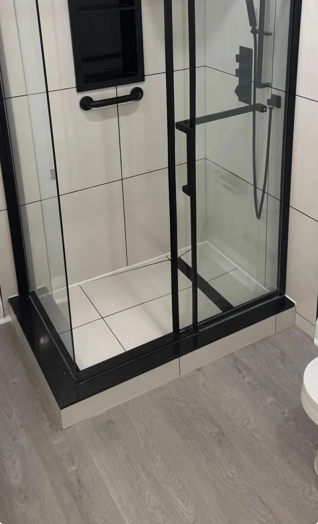 Black-framed glass shower with a tiled base and wall niche