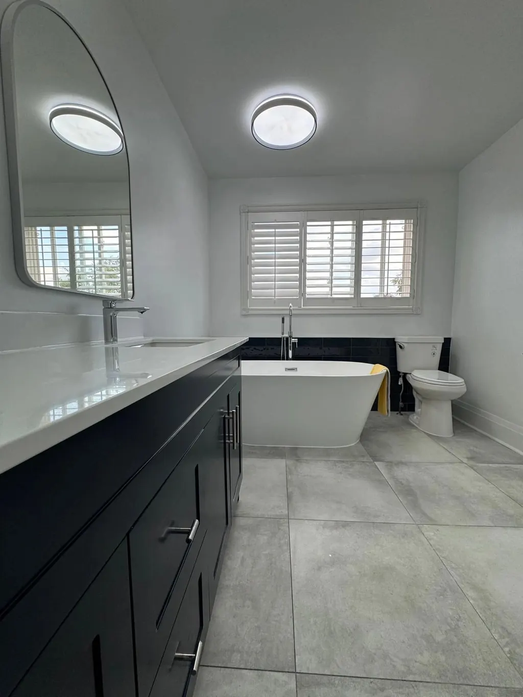 Full bathroom renovation with a black double vanity, freestanding tub and large-format floor tile
