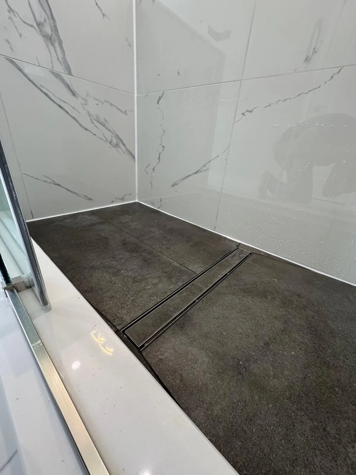 Linear drain shower base in dark floor tile with white marble-look walls