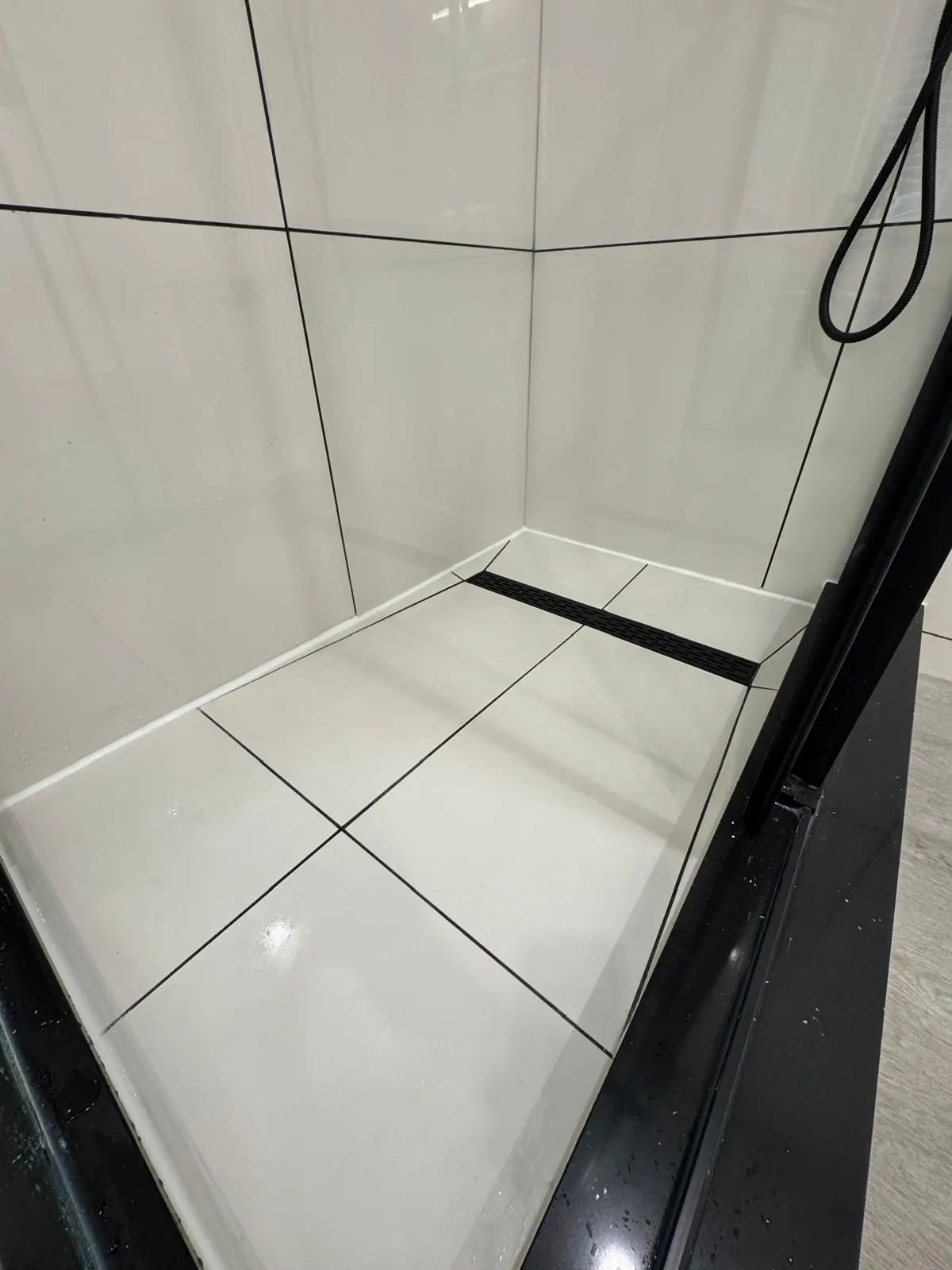 Linear drain shower base in large-format white tile with dark grout lines