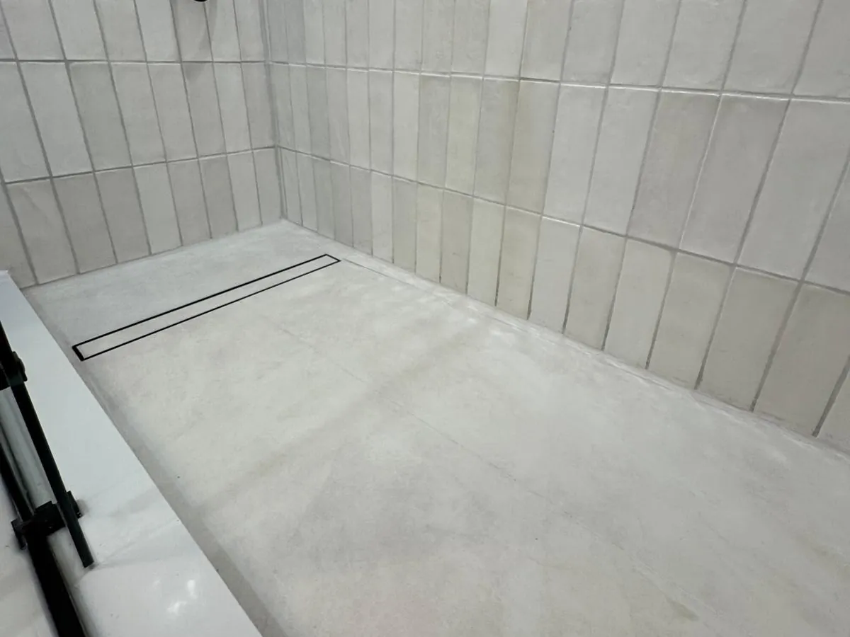 A Canzeno tiled shower base with a linear drain, installed in a white-tiled shower